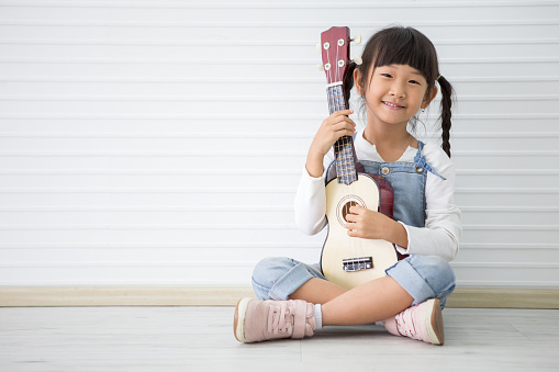 little asian girl sitting playing ukulele on white background with copy space