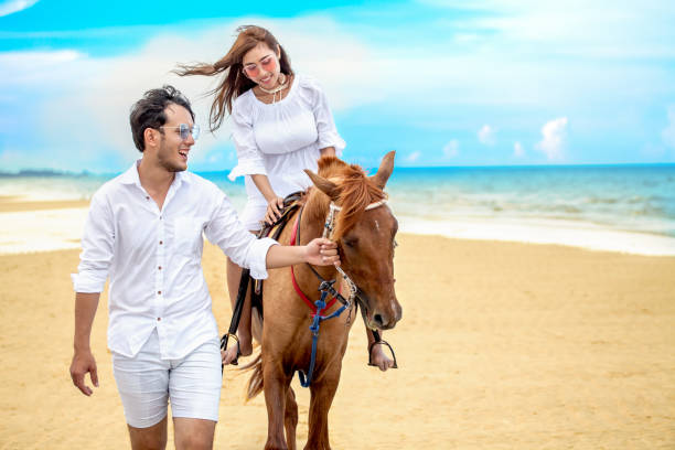 jovem casal apaixonado andando com o cavalo na praia do mar no céu azul. férias de verão tropical mar-de-mel. noiva noivo ao cavalo - honeymoon wedding beach couple - fotografias e filmes do acervo
