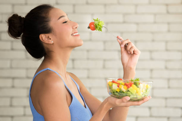 アジアの女性の側にサラダ ボウルとうれしそうな姿勢で - women eating fruit food ストックフォトと画像