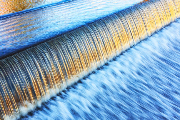 Silky Golden Light on Lake Placid New York Evening Waterfall This Chubb River and Upper Mill Pond barrier waterfall is located near the intersection of Station Street and Sentinel Road in the center of the village of Lake Placid, New York. The calm, lazy pond surface to the left is rippled and serene. Early evening golden sunlight highlights infinite silky smooth ribbons of speeding water spilling over the edge and slipping down into that long, continuous rush of blurred, streaking splashes. Shot with Canon EOS 5D Mark II body and Canon EF 70-200mm f/2.8L USM lens.

NOTE: I thought the light was perfect, so this is one of a series of several images shot within a few minutes exploring different aperture and shutter speed settings. There are also various post-processing/cropping combinations in the group. This one is 1/25 shutter speed with an aperture of F/11. Horizontal composition. fast water stock pictures, royalty-free photos & images