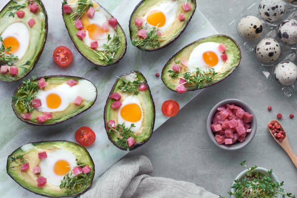 istock Keto diet dish: Avocado boats with quail eggs, ham cubes and cress sprouts on light stone serving board 1090523114