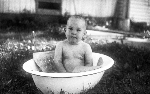Baby bathes in a small plastic tub in the garden. Kid having fun, splash water and laughs. Summer, vacation, health.