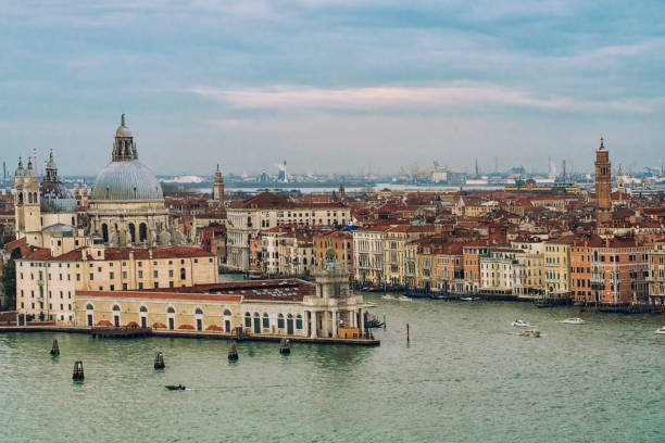 High angle view on venetian lagoon with St. Mark's square. Time of Venice Carnival with large group of people on water's edge.