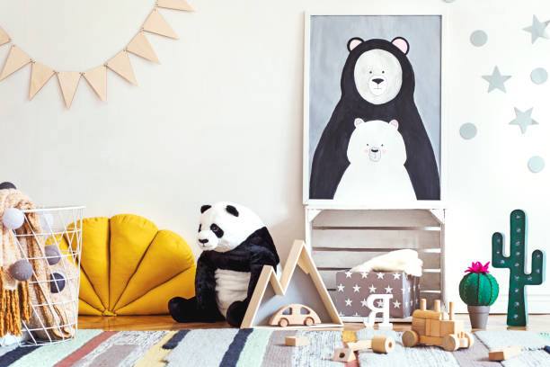 istock Stylish scandinavian kid room with mock up poster frame on the pattern wall, boxes, teddy bear and toys. Cute modern interior of playroom with white walls. 1090539356