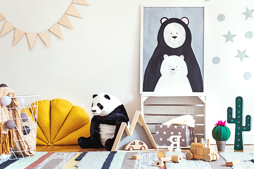 Stylish scandinavian kid room with mock up poster frame on the pattern wall, boxes, teddy bear and toys. Cute modern interior of playroom with white walls.