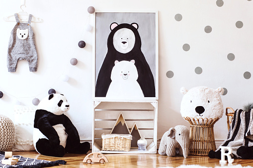 Scandinavian kid room with mock up photo frame on the pattern wall, boxes, teddy bear and toys. Cute modern interior of playroom with white walls, wooden accessories and colorful toys.