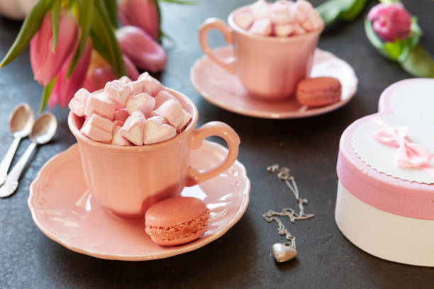 istock Two pink cups with pink heart shaped marshmallows with macaroons, pink tulips,  gift box and silver heart shape pendant on chain. Romantic breakfast for two. Close-up, selective focus. 1090547290