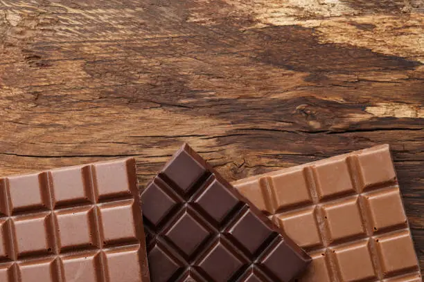 Various square shape chocolate bars on brown wooden background, top view