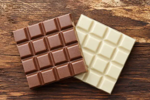 Milk and white square shape chocolate bars on textured brown wooden background, top view