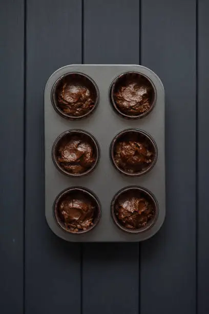Batter for homemade chocolate muffins in baking tray on dark background top view copyspace