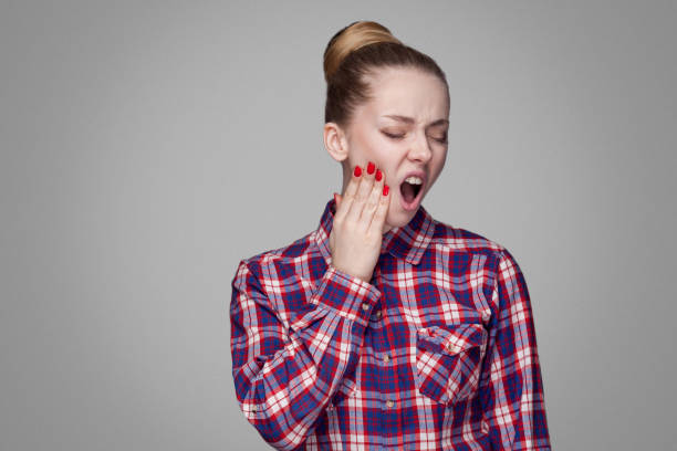 dor de dente. menina loira infeliz na camisa quadriculada de vermelha, rosa, coletados penteado coque, maquiagem permanente tocando seu dente doloroso com a boca aberta - shirt problems red pink - fotografias e filmes do acervo