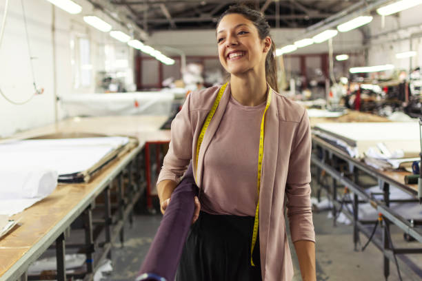 smiling young woman in a fashion factory - textile textile industry warehouse store imagens e fotografias de stock