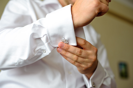 Man buttons cuff link on the shirt.