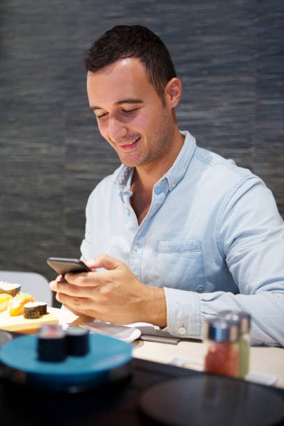 istock happy man sitting at sushi restaurant with mobile phone 1090648582