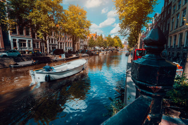istock Channel in Amsterdam in autumn sunlight. Boat floating tree-lined canal, vibrant reflections, white clouds in the sky. Netherlands houses landmark landscape 1090757354