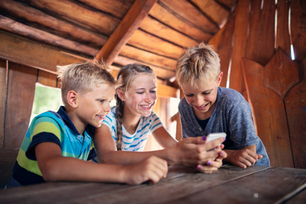 Three kids playing with smartphone inside of a tree house Three kids playing with smartphone inside of a tree house. 
Nikon D850 summer camp cabin stock pictures, royalty-free photos & images
