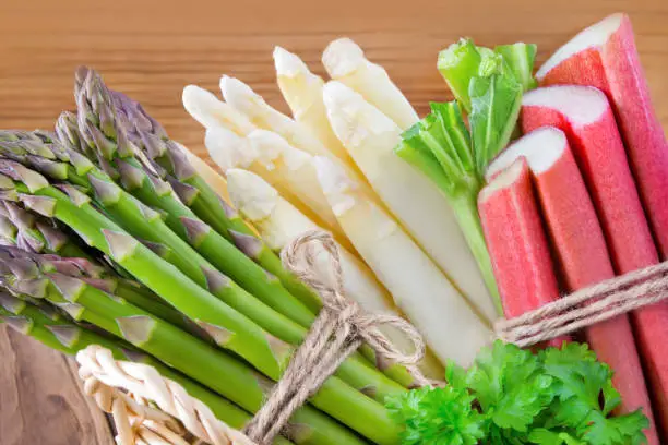 Green and white asparagus with rhubarb against wooden background
