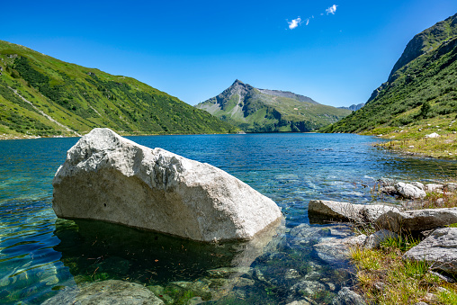 Large dammed lake in the mountains Austria with large white stones and rocks in the sun.