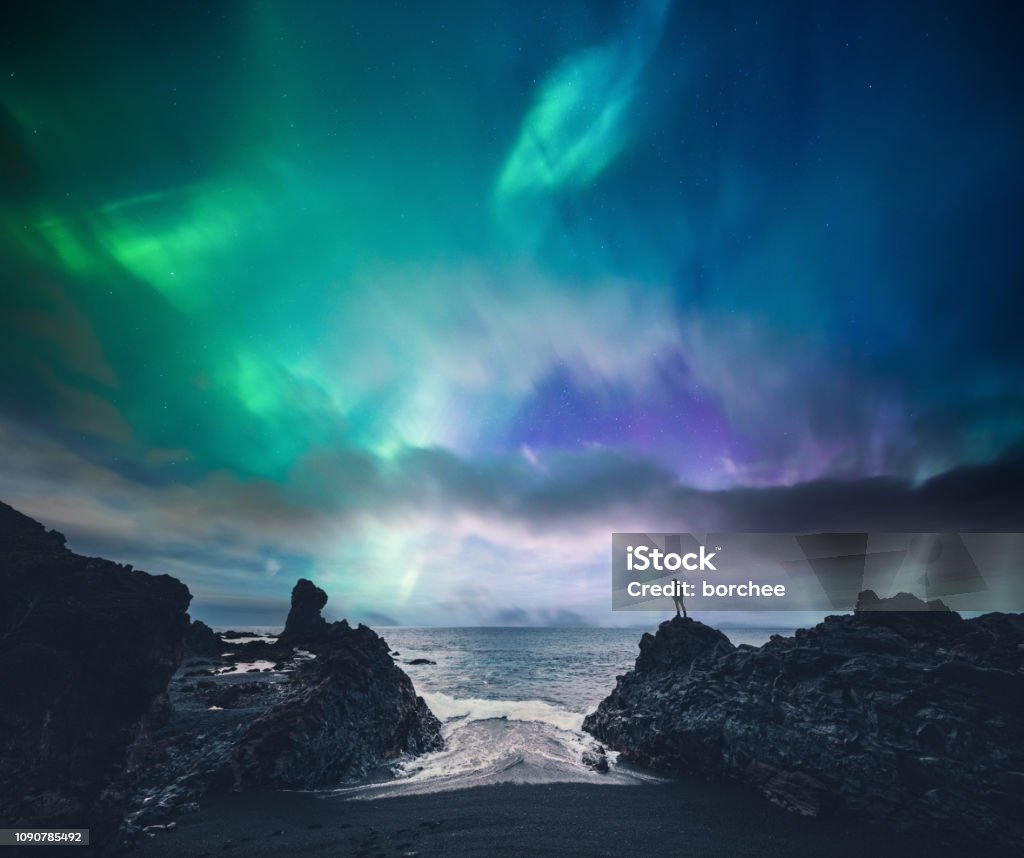 Amazing Iceland Man standing on the rock at the beach watching northern lights (Iceland). Aurora Borealis Stock Photo