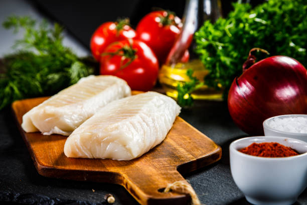 свежее сырое филе трески на разделоной доске - cod fillet raw prepared fish стоковые фото и изображения