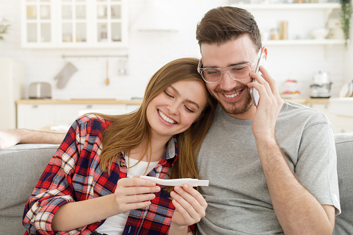 Happy couple with positive ovulation test calling relatives or friends to share great family news