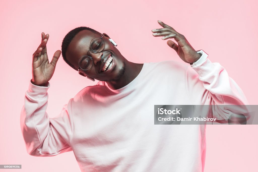 Young handsome african american man dancing, singing his favorite song with closed eyes, isolated on pink background Music Stock Photo