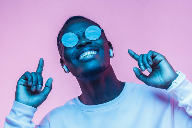 jeune homme afro-américain souriant, écouter de la musique avec des écouteurs, danse isolée sur fond rose - men fashion model cool glasses photos et images de collection