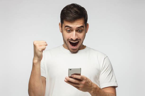 happy guy holding smartphone having won something in internet, perhaps in online casino - smiling casino human hand beautiful imagens e fotografias de stock