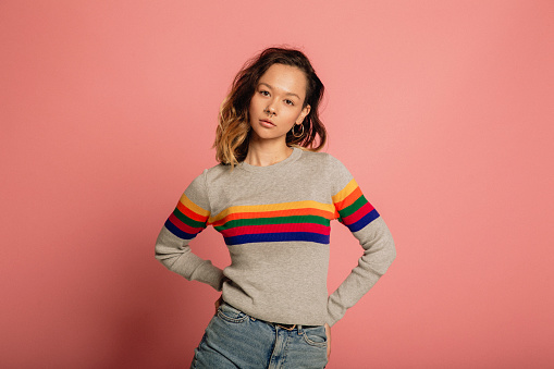 Young woman dressed in a striped sweater in front of a pink background.