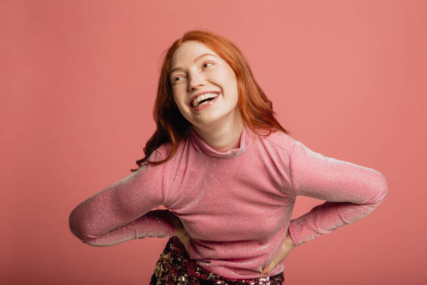Just Being Herself Close-up portrait of a young redhead woman dressed in a pink sparkly top standing in front of a pink background. redhead photos stock pictures, royalty-free photos & images