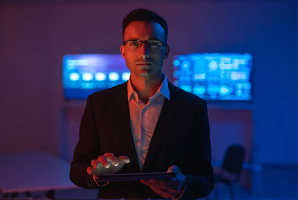 The man in glasses with a tablet working in a room with screens stock photo