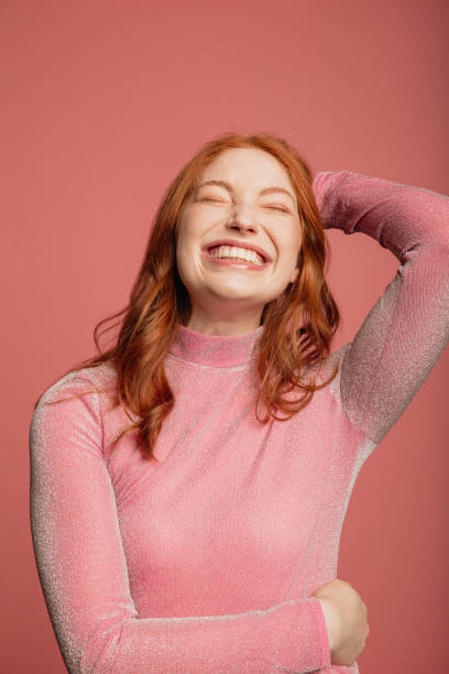 Headshot of a Smiling Redhead Close-up portrait of a young redhead woman dressed in a pink sparkly top standing in front of a pink background. redhead photos stock pictures, royalty-free photos & images