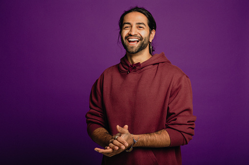 Portrait of a handsome Asian man wearing a purple hoodie standing in front of a purple background.