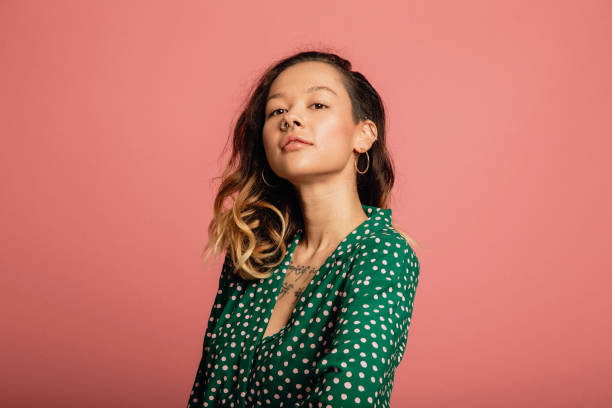 Portrait of a Beautiful Woman Young woman dressed in a green polka dot shirt standing in front of a pink background. tattoo photos stock pictures, royalty-free photos & images