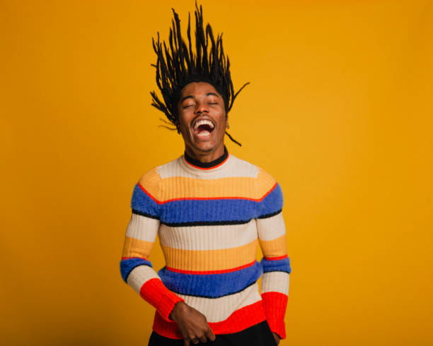 Flipping His Hair Waist-up portrait of a young man flipping his hair in front of a yellow background. He is wearing a striped sweater. dreadlocks stock pictures, royalty-free photos & images