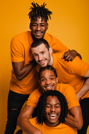 Mixed race group of friends creating a human pyramid. They are all wearing yellow and are standing in front of a yellow background.