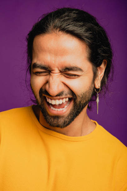 Uncontrollable Laughter Portrait of an Asian man laughing, he is standing in front of a purple background and wearing a yellow sweater. men close up 20s asian ethnicity stock pictures, royalty-free photos & images