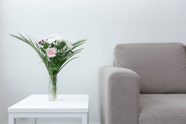 Couch next to table of flowers modern living room decor against white background stock photo