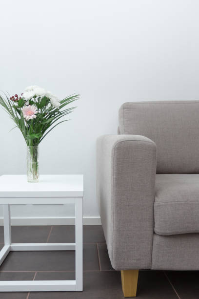 Couch next to table of flowers modern living room decor against white background vertical stock photo