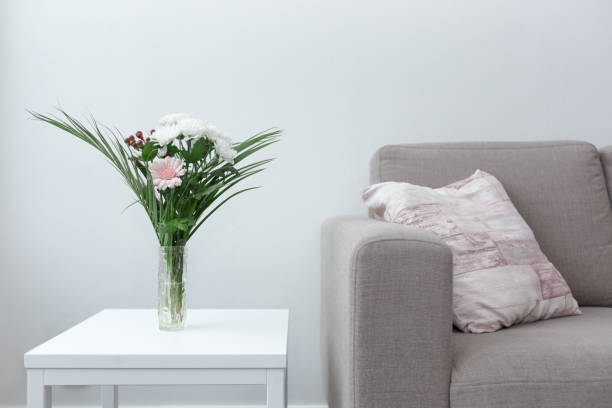 Couch with pillow next to table of flowers modern living room decor against white background stock photo