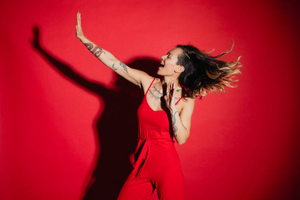 Having the Time of Her Life Young woman dressed in a red jump suit dancing in front of a red background. tattoo photos stock pictures, royalty-free photos & images
