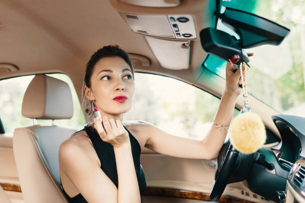istock Young elegant woman looking in the car view mirror while applying makeup, lipstick on the lips 1090862572