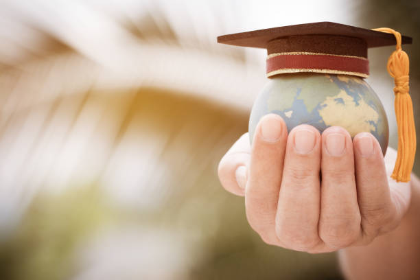 Graduate or Education knowledge learning study international abroad concept : Graduation cap on opening textbook with blur earth world globe model map in outdoor of campus, Back to School stock photo