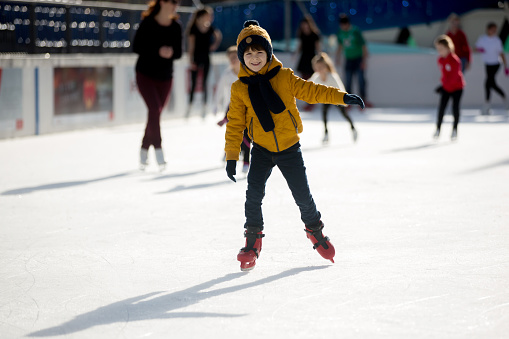 Happy boy with hat and jacket, skating during the day, having fun outdoors, winter time on Christmas