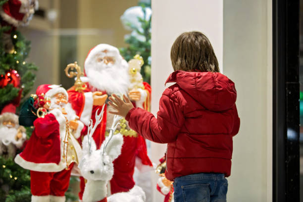 красивый маленький ребенок, мальчик, наблюдая за рождественским украшением с игрушками в витрине магазина, желая подарок - место представляющее интерес стоковые фото и изображения