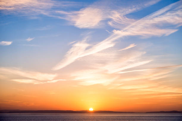 Beautiful sunrise in orange colors, sun, a blue sky with interesting cloud formation and the sea.