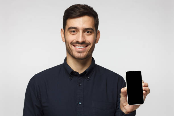 istock Smiling handsome young man holding smartphone with  blank screen, isolated on gray background 1090878266