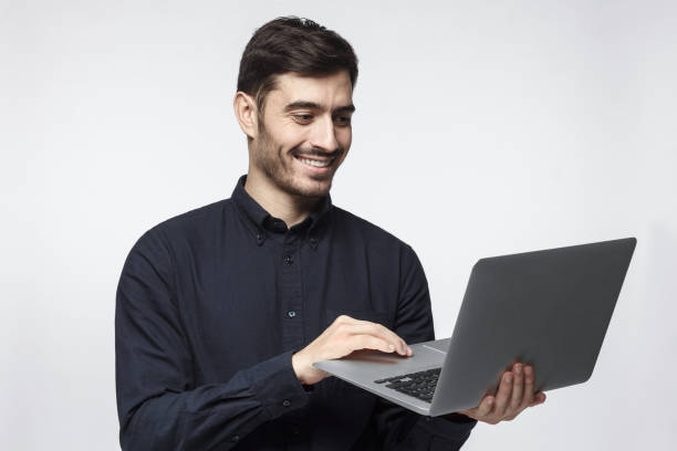 istock Young modern businessman standing, holding laptop with happy smile, using touchpad 1090878362