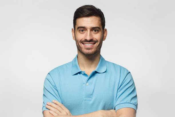 retrato de homem bonito na camisa polo azul, de pé com os braços cruzados, isolados no fundo cinza a sorrir - blue polo shirt - fotografias e filmes do acervo