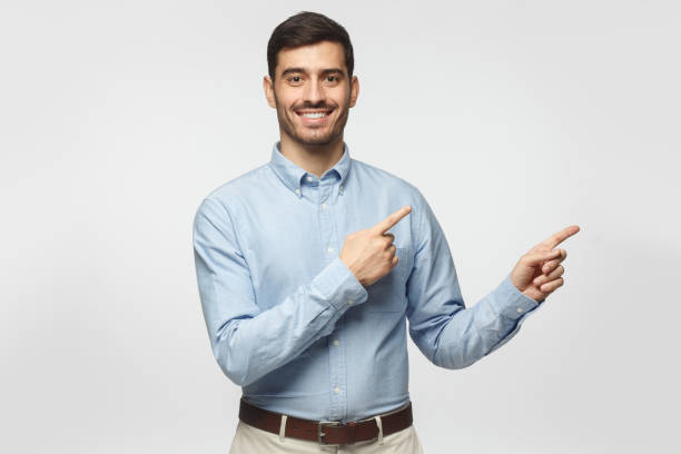 smiling businessman pointing right with two hands and looking at camera, isolated on gray background - gesturing business looking at camera caucasian imagens e fotografias de stock
